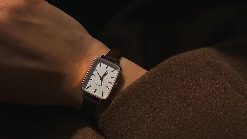 A simple analog watch on a wrist, lit by low afternoon sun against a wool coat.